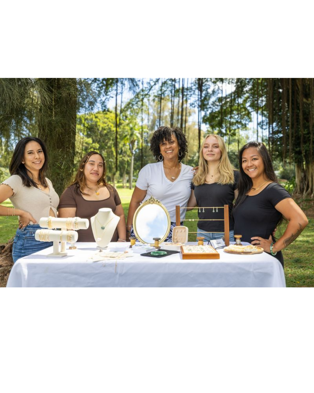 Five women standing behind a table with jewelry display outdoors